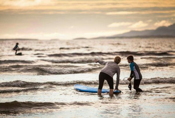 ocean scene with one adult and child looking to horizon with surfboard, little waves